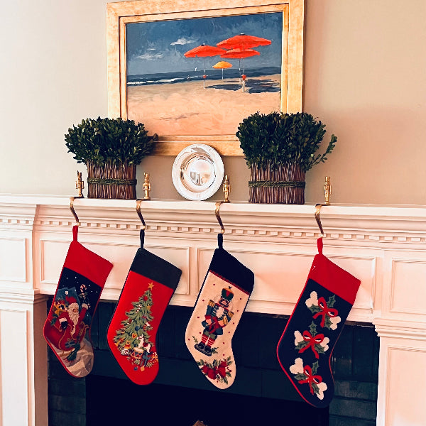 Three Christmas stockings hanging on a fireplace, decorated with festive designs including Santa Claus, a Christmas tree, and holiday-themed embroidery.