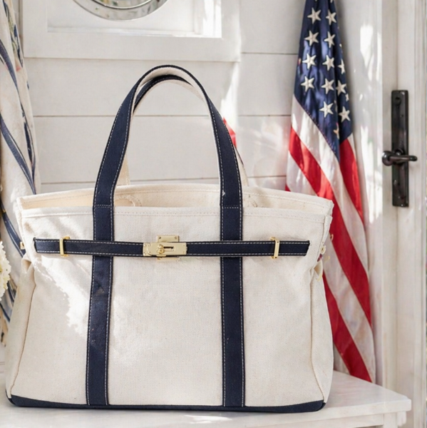 White tote bag with navy straps on a white surface with an American flag in the background.