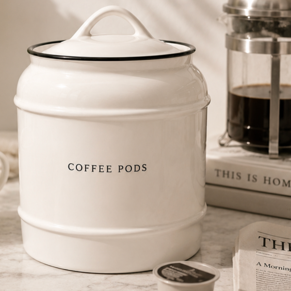 White container labeled 'Coffee Pods' on a marble surface with a French press in the background.