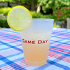 Clear plastic cup with 'GAME DAY' text on a checkered tablecloth, garnished with a lemon slice.
