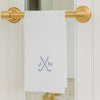 White towel with monogram hanging on a gold towel rack against a white door.
