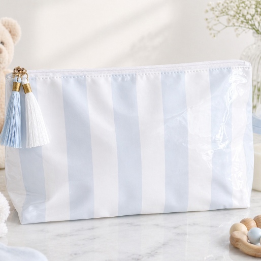 White and blue striped bag with tassels on a light surface with a teddy bear and toys in the background.