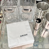 A set of white cocktail napkins with the word 'DRINK' printed on them, displayed on a table with glassware and metalware in the background.