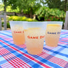 Two 'Game Day' cups on a blue and red checkered tablecloth with trees in the background.