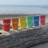 Colorful cups labeled 'BEACH' on a wooden log at the beach.