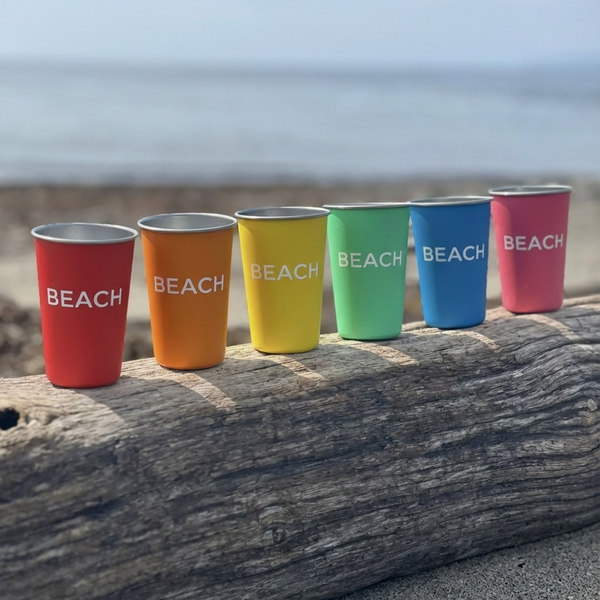 Colorful cups labeled 'BEACH' on a wooden log at the beach.