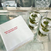 A set of paper napkins with the text 'HAS ANYONE SEEN MY CONTRACTOR?' printed on them, displayed on a table with two glasses of martini.