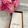 Pink flowers in a vase next to a napkin with text on a marble surface