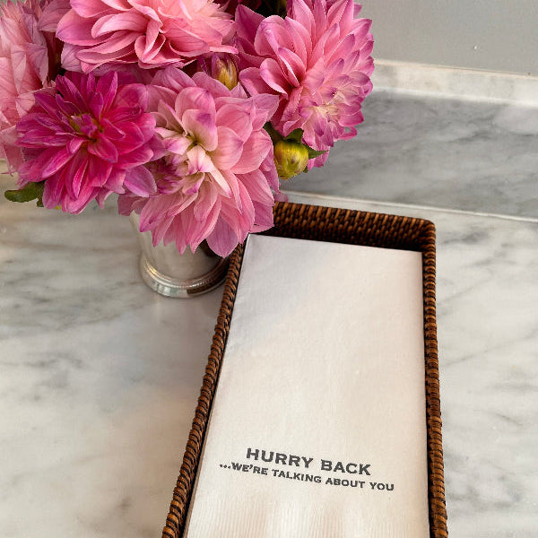 Pink flowers in a vase next to a napkin with text on a marble surface
