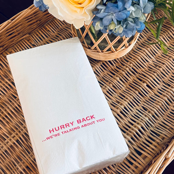 Folded white napkin with red text on a wicker surface with flowers in the background