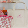 Beige tote bag with 'SALLY' branding on a shelf with beauty products.
