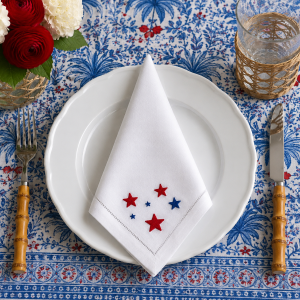 Table setting with white plates, napkin with star pattern, and floral centerpiece on a blue patterned tablecloth.