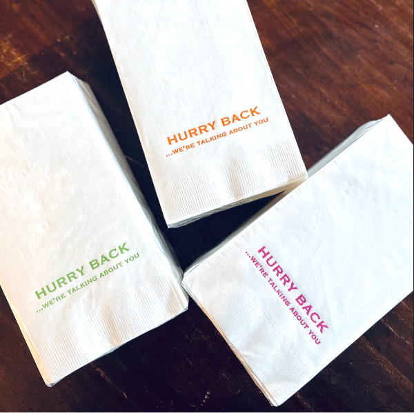 Three white napkins with text on a wooden surface