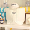 White tote bag, cap, and beach towels with 'Georgia Beach' branding on a shelf.