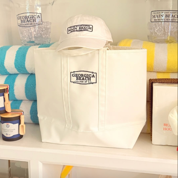 White tote bag, cap, and beach towels with 'Georgia Beach' branding on a shelf.
