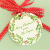 Round Christmas gift tag with green wreath design, red berries, and red ribbon on a light green background.