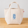 Beige tote bag with a blue and white logo on a wooden surface