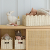 Children's room with wooden shelf, wicker baskets, and toys against a light gray wall.