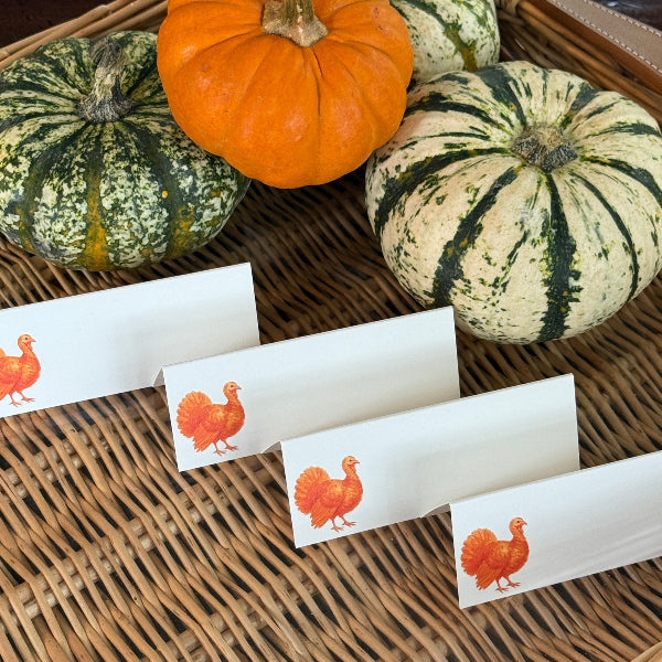 Pumpkins and gourds on a woven surface with Thanksgiving-themed place cards featuring turkeys.