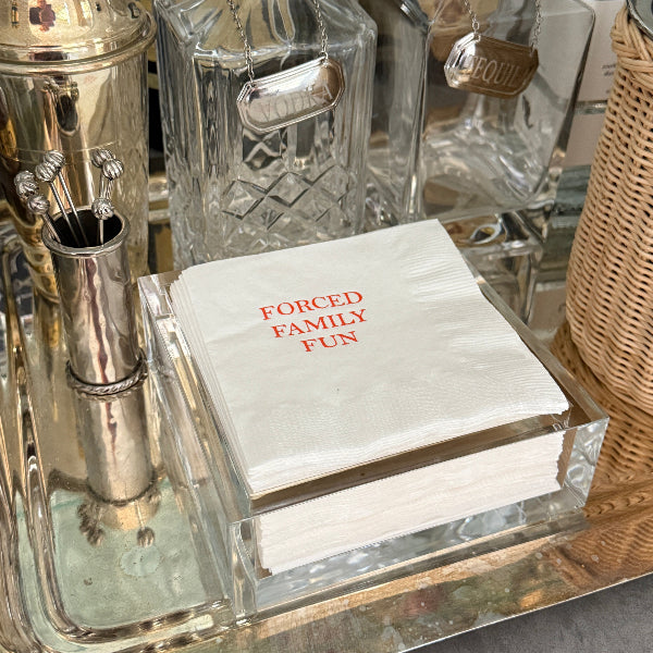 Alcohol bottles and a cocktail shaker with a napkin reading 'FORCED FAMILY FUN' on a bar counter.