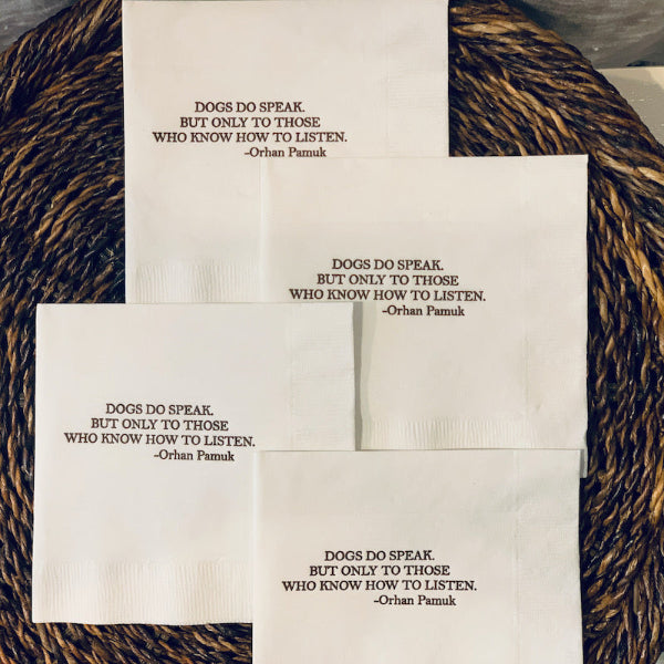 A set of white cocktail napkins with brown text, featuring a quote about dogs understanding humans.