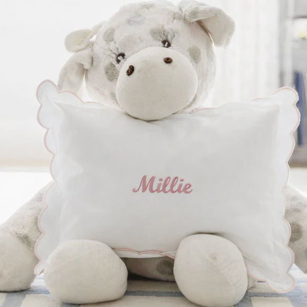 Plush toy cow with a pillow that has 'Millie' embroidered on it, on a light background.