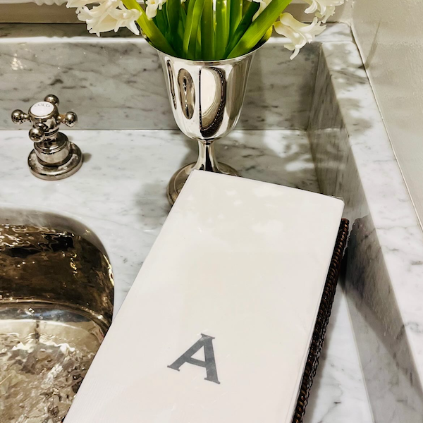 A monogrammed hand towel with the letter 'A' displayed on a sink counter, next to a vase with flowers.
