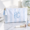 Marble-patterned pouch with 'HC' initials, tassel, and makeup items on a marble surface.