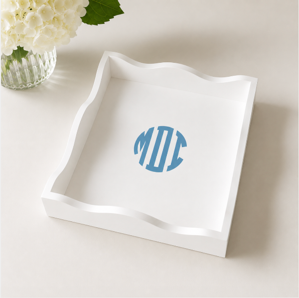 White decorative tray with blue monogram on a light surface with flowers.